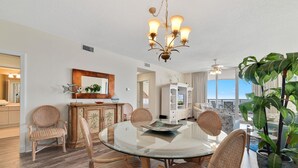 A dining area with a glass table, wicker chairs, a chandelier, and a view of the ocean.