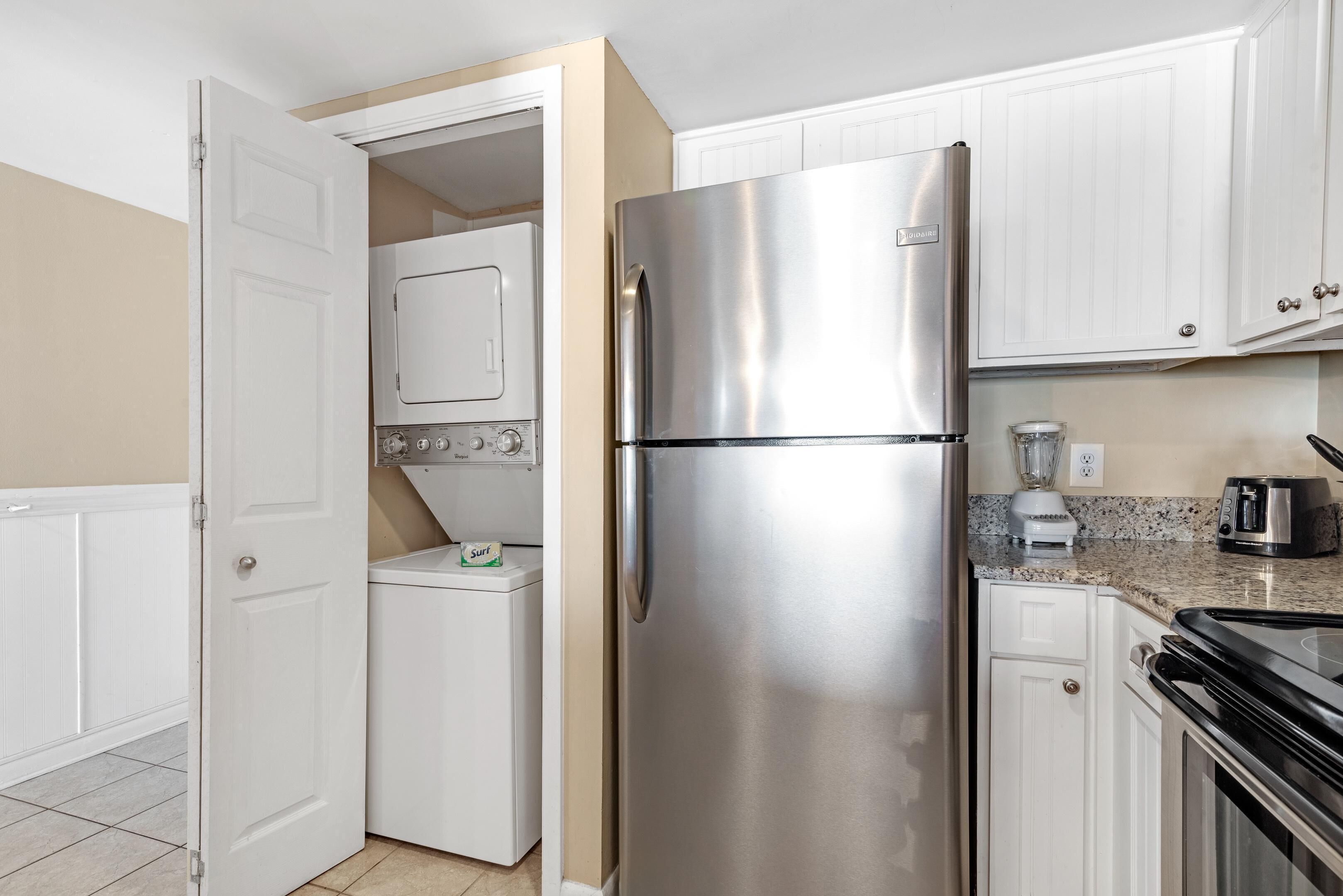 Une cuisine compacte dotée d’un réfrigérateur en acier inoxydable, d’un appareil combiné lave-linge et sèche-linge intégré et d’un plan de travail en granit.
