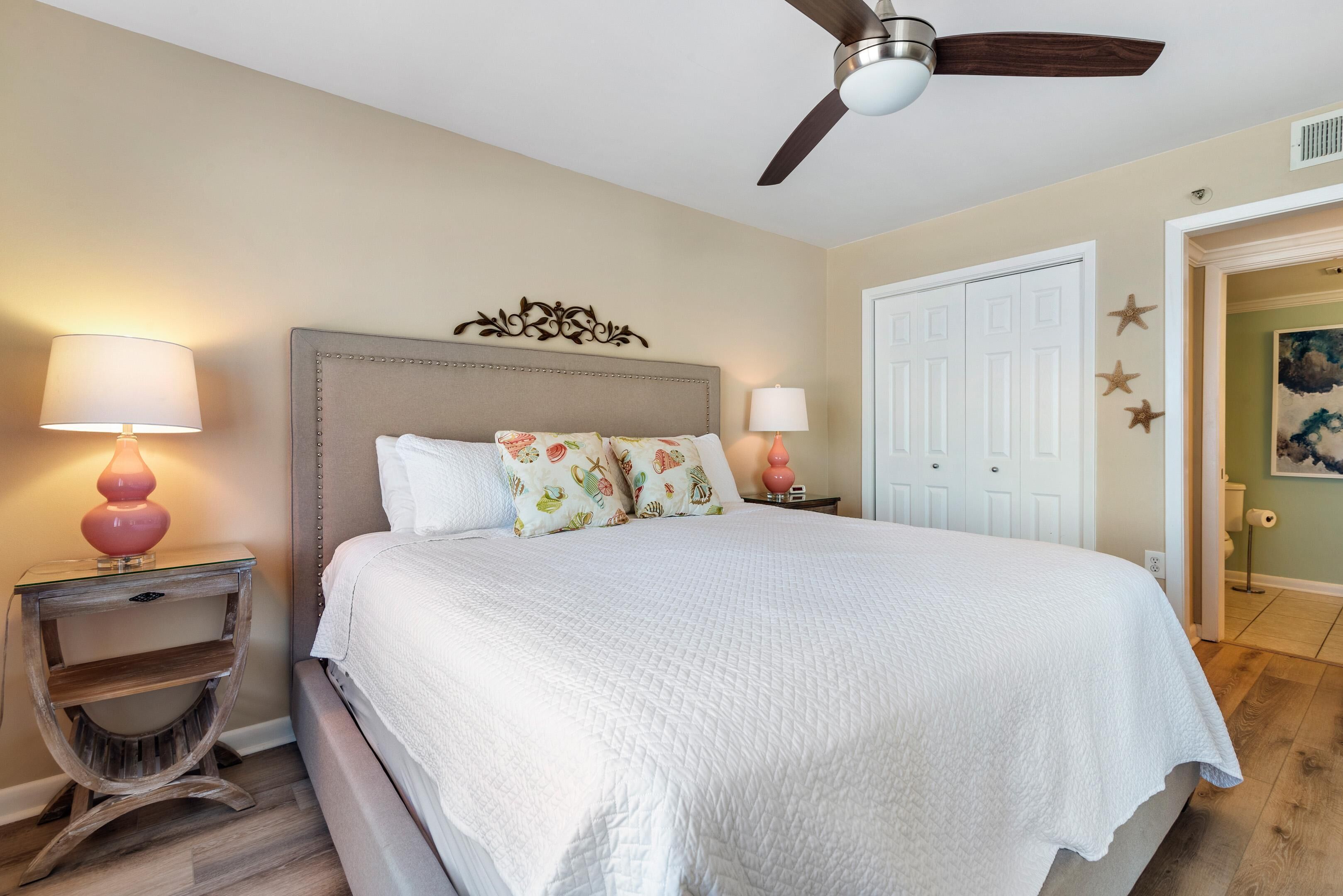 A bedroom with a bed, two bedside tables with lamps, a ceiling fan, and a door with star decorations.