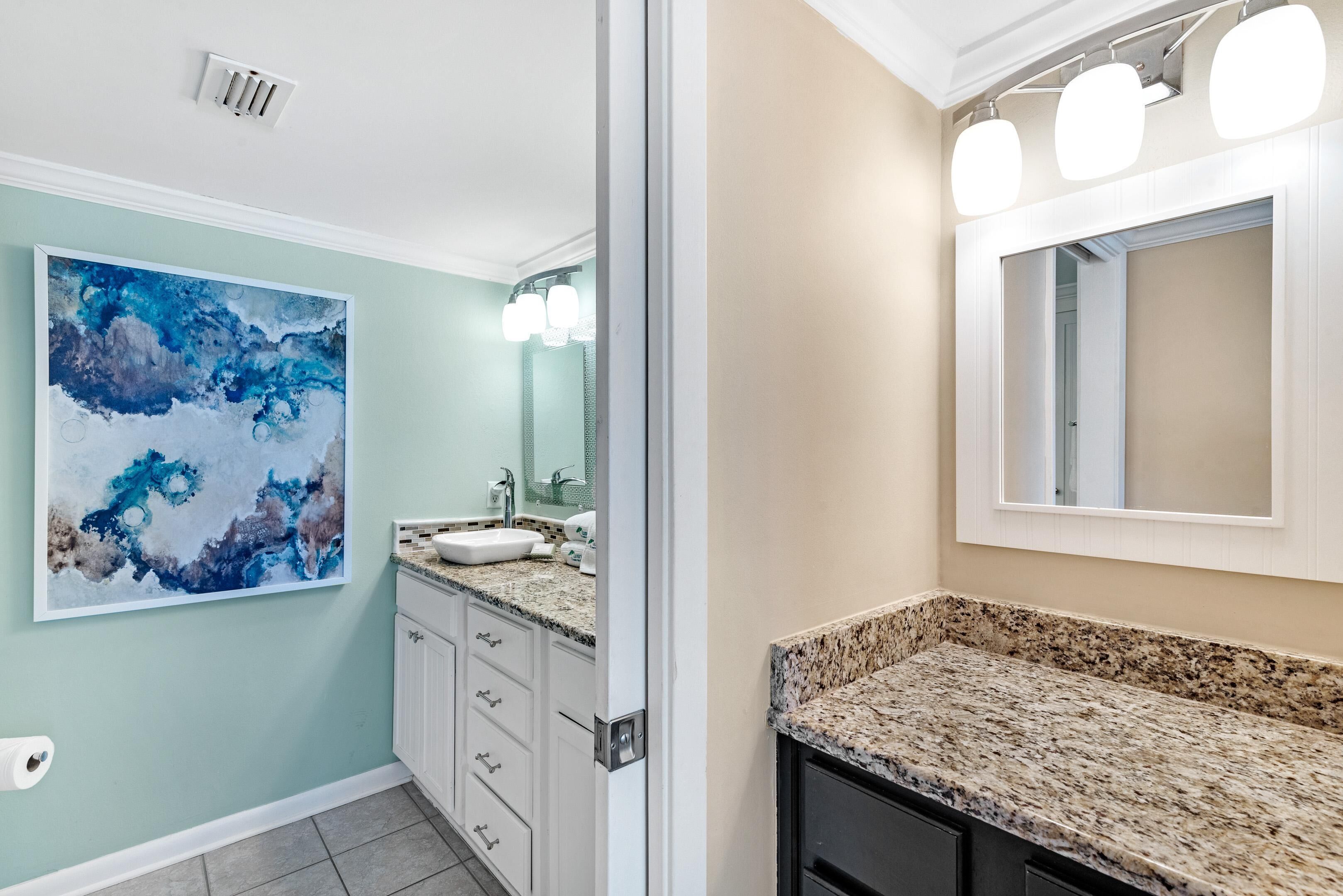 Une salle de bain dotée d’un comptoir en granit, d’un lavabo, d’un grand miroir et d’un luminaire fixé au mur.