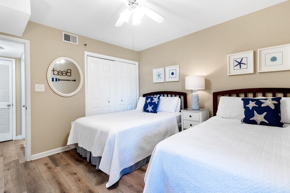 A bedroom with two beds, a ceiling fan, a white door, and wall art.