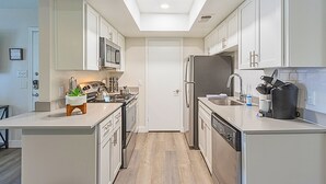 Una cocina moderna con armarios blancos, una isla central, horno empotrado y refrigerador.