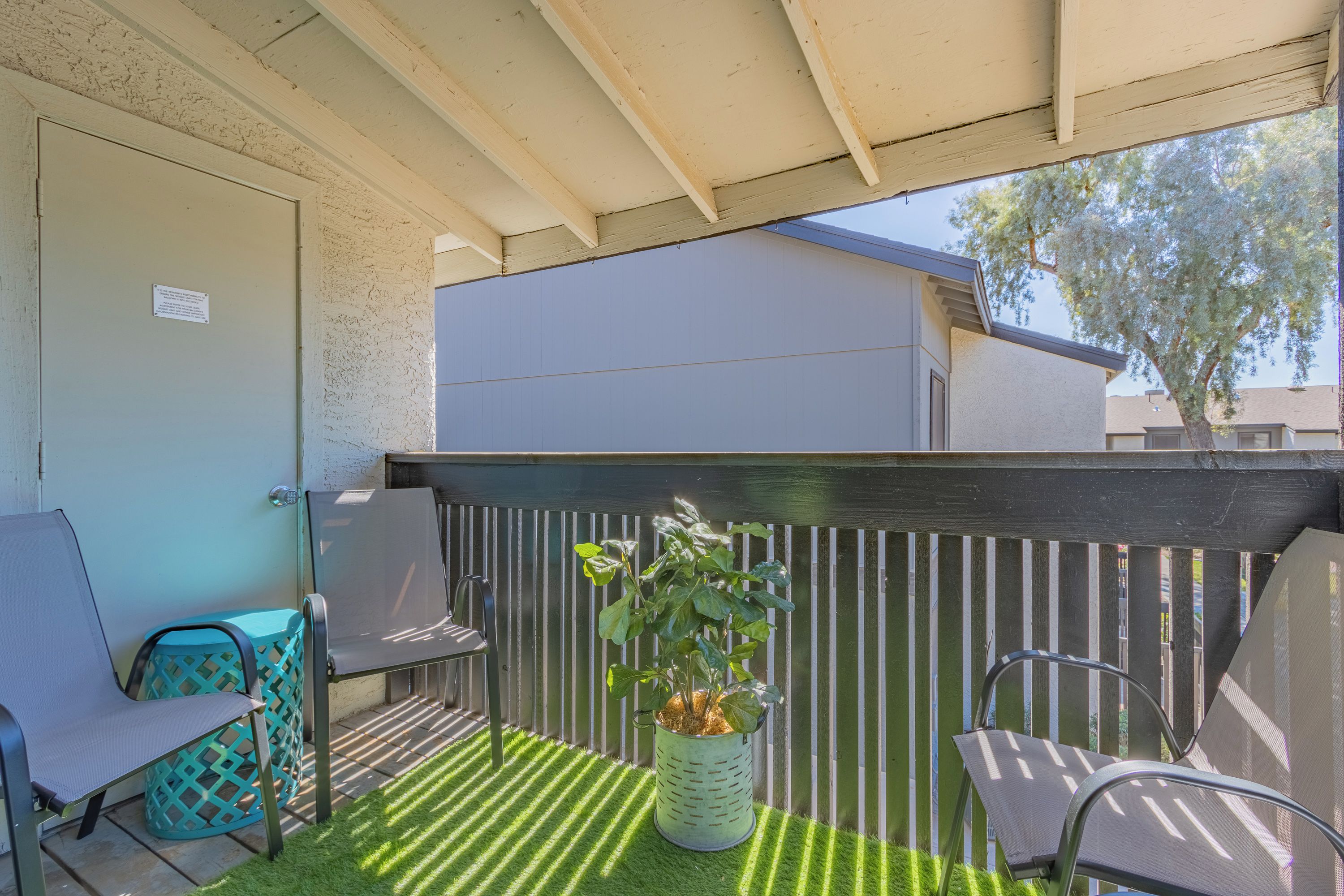 A patio with two metal chairs, a potted plant, and a green artificial turf.
