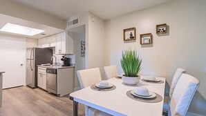 Una cocina compacta con electrodomésticos modernos, un comedor con una mesa y sillas blancas, y una pequeña planta en maceta en la pared.