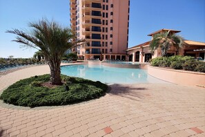 A hotel with a swimming pool, palm trees, and a brick-paved area. - Seachase 905c (Orange Beach)
