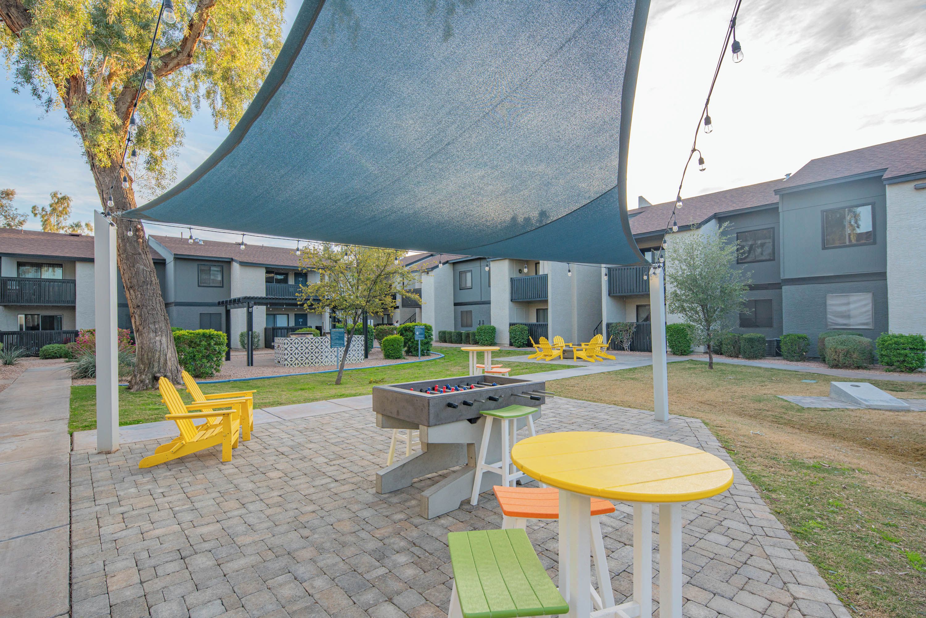 An outdoor patio area with a foosball table, seating, and a shaded area.