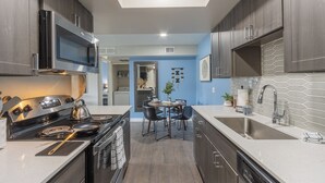 Een moderne keuken met donkere kastjes, roestvrijstalen apparatuur, een eethoek met een ronde tafel en stoelen, en uitzicht op de aangrenzende woonruimte.