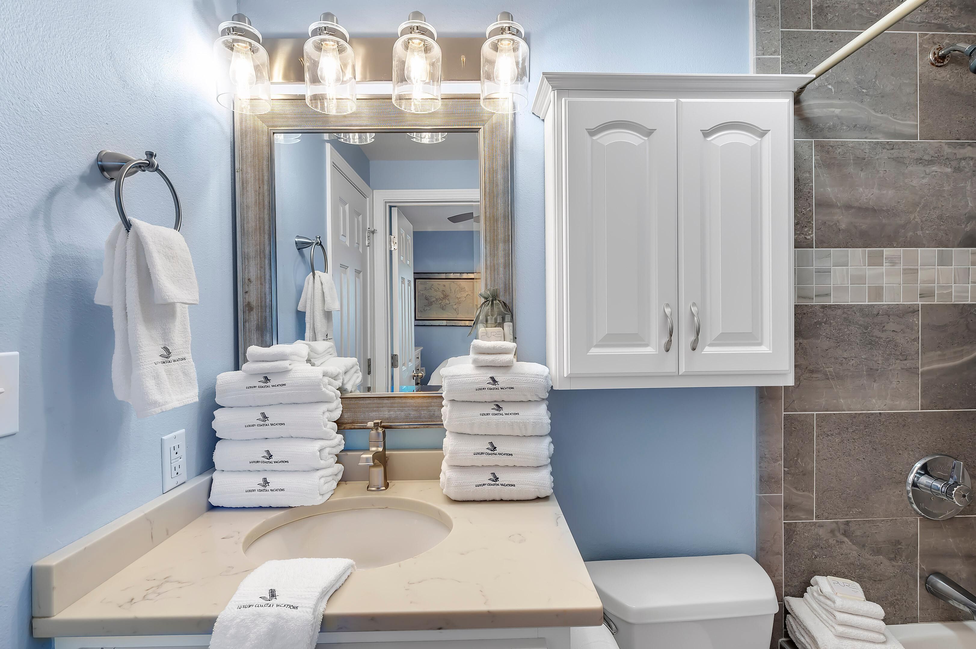 Un baño con lavamanos, espejo y muebles blancos.