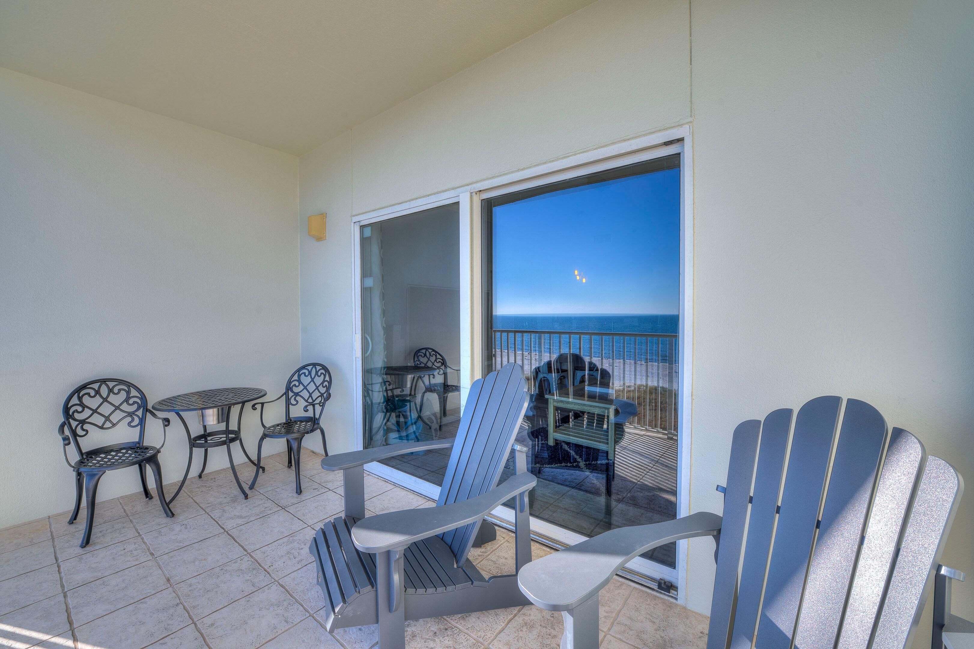 A balcony with a view of the ocean, featuring a table, chairs, and a chair.