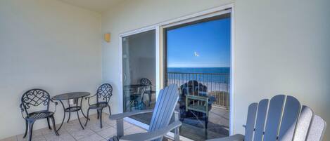 A balcony with a view of the ocean, featuring a table, chairs, and a chair.