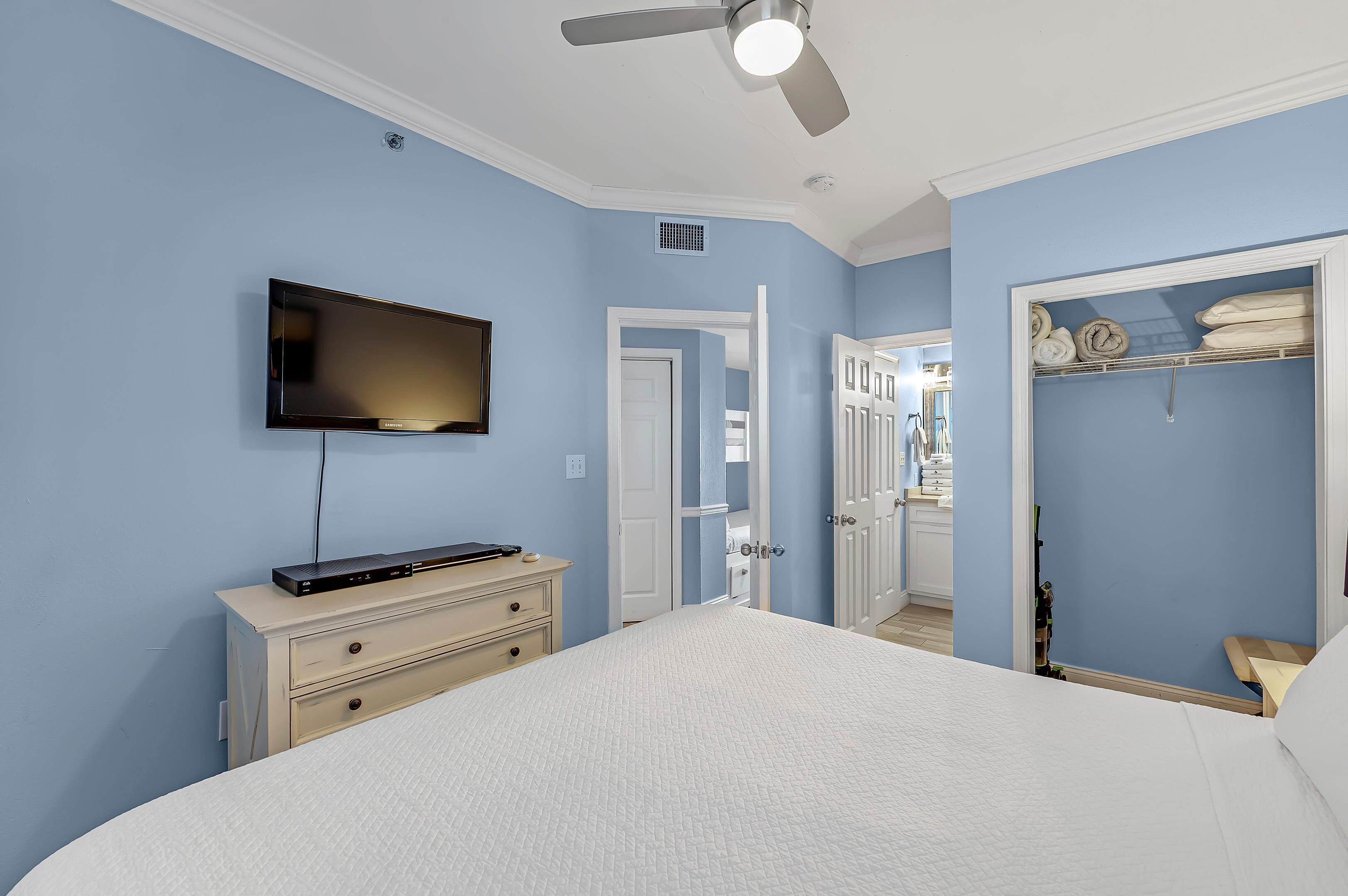 Une chambre à coucher comprenant un lit, un téléviseur fixé au mur, une commode et un placard.