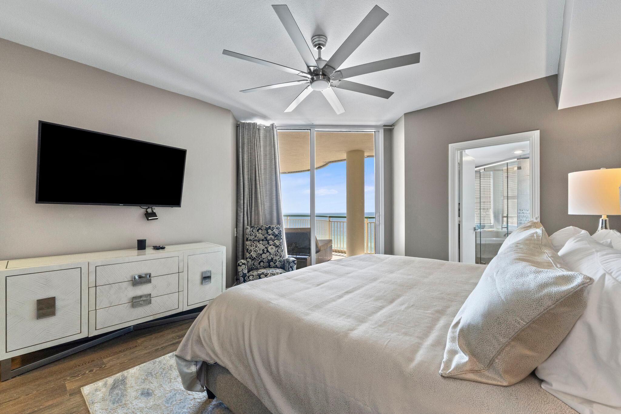 Un dormitorio moderno con una cama grande, ventilador de techo, televisión, vistas al balcón y vestidor.