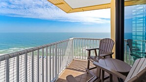 A balcony with a view of the ocean, wooden chairs, and a glass railing. - Summer House 1501b (Orange Beach)