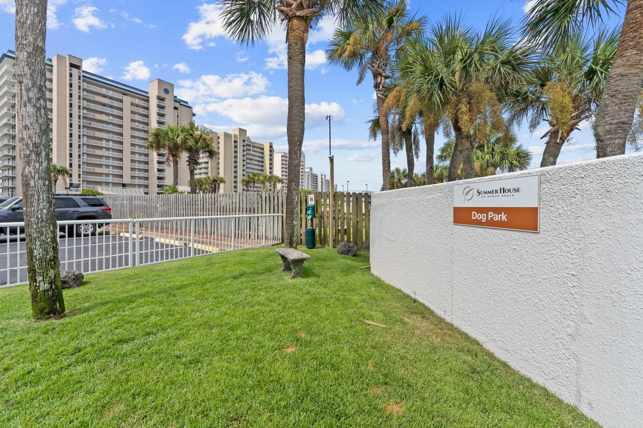 A grassy area with a stone bench, palm trees, and a sign for 'Dog Park' at Summer House on Roman Beach.