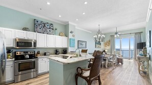 A modern kitchen with white cabinets, stainless steel appliances, and a central island with bar stools. - Spanish Key 702 (Pensacola)