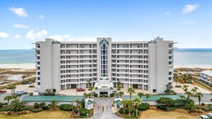 A large, multi-story hotel with a central entrance, surrounded by a parking area and palm trees. - Spanish Key 702 (Pensacola)