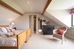 A bedroom with a sloped ceiling, a bed with a wooden headboard, a wicker chair, a dresser, and a mirror.