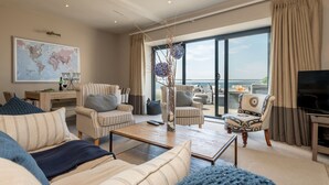 Un vaste salon doté d’une grande fenêtre donnant sur un balcon, et aménagé avec des canapés et des fauteuils à rayures, ainsi qu’une table basse.