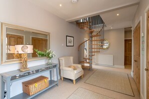 A room with a wooden staircase, a console table, a chair, and a large mirror.