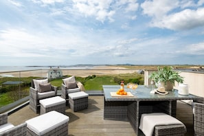 A deck with wicker furniture, a table with drinks, and a view of the beach.