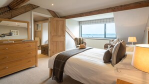 Une chambre avec un grand lit, une commode en bois et une vue sur la mer par la fenêtre.