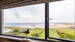 Une pièce dotée d’une grande fenêtre donnant sur une plage et une maison blanche.