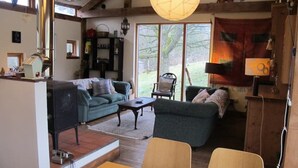 Uma sala de estar acolhedora com sofá, mesa de centro e mesa de jantar. Há uma janela grande que oferece luz natural e vista para o exterior.