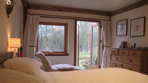 Quarto com cama, uma cadeira, cômoda e janela com cortinas.