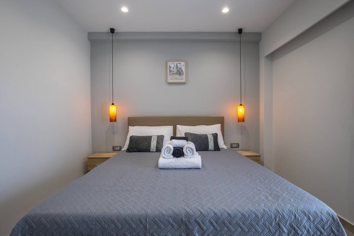 A neatly made bed with a grey quilt, two bedside lamps, and a framed picture on the wall.