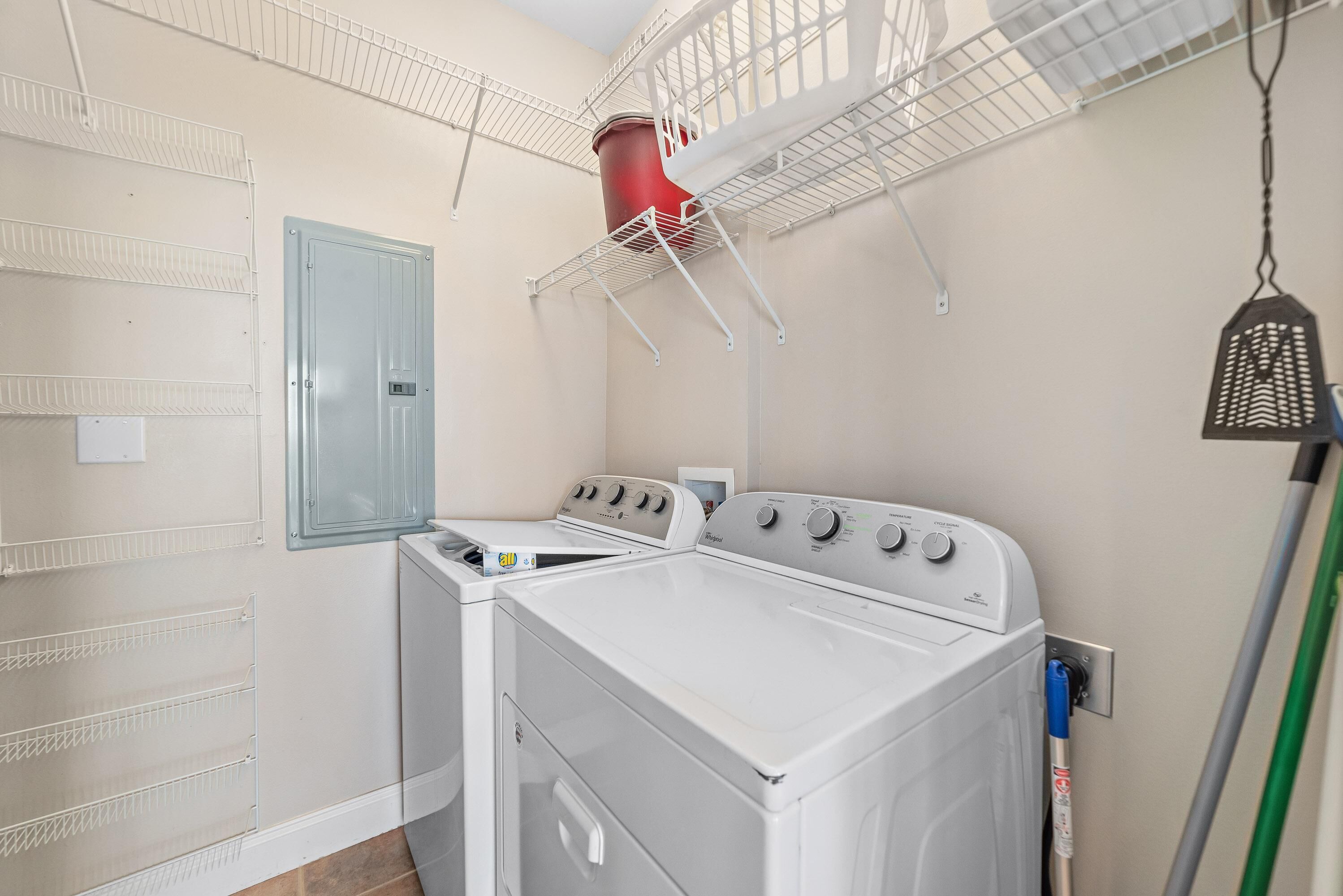 A laundry room with a front-loading washer and dryer, metal shelving units, a blue door, and a hanging light fixture.
