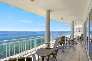 A balcony with a view of the ocean, furnished with chairs and tables.