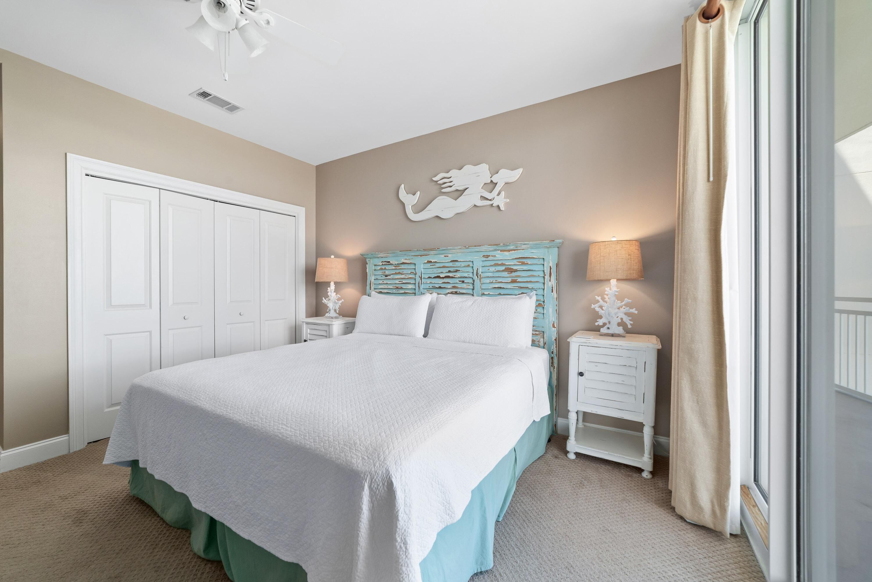 A bedroom with a large bed, white headboard, two bedside tables with lamps, a decorative wall piece, and a door.