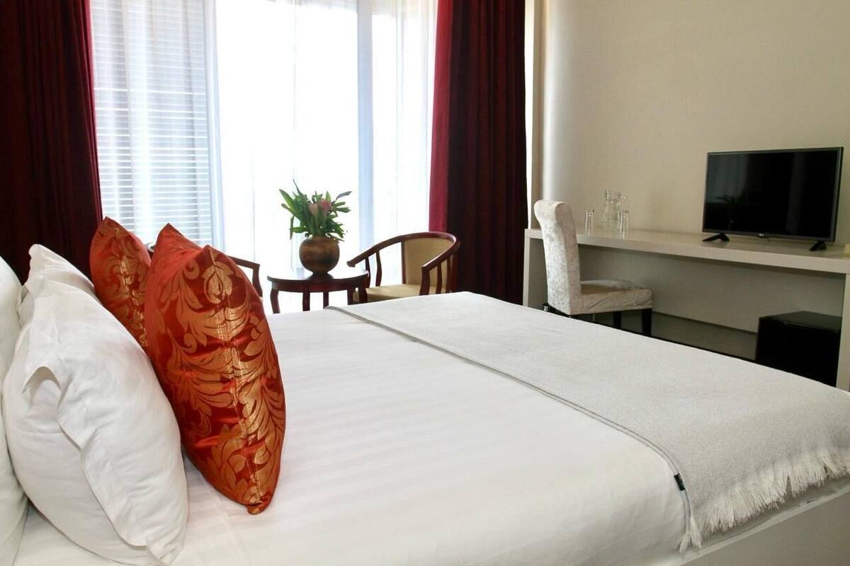 Una habitación de hotel con una cama, un escritorio con televisor, una silla y una mesita con planta.