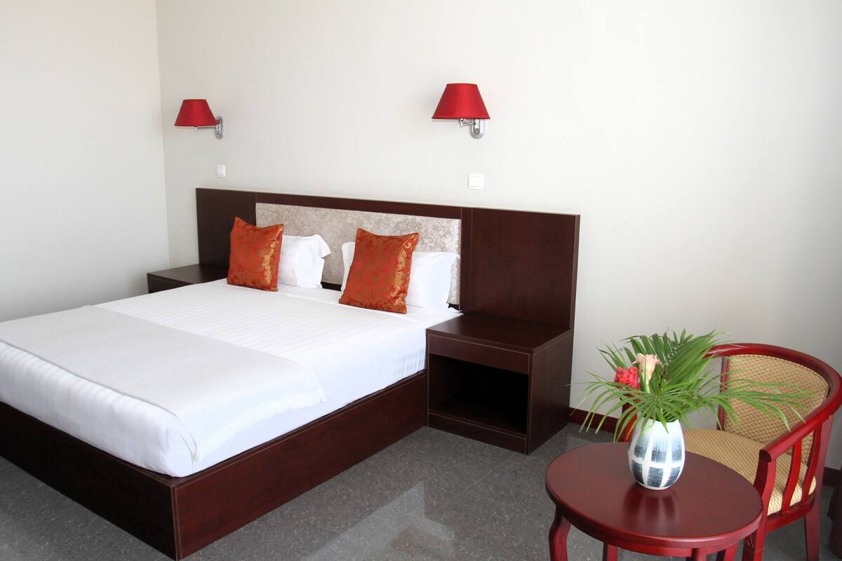 Habitación de hotel con una cama grande, dos mesitas de noche, una pequeña mesa con un florero y dos lámparas de pared.