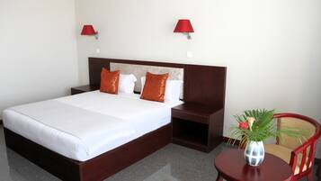 Habitación de hotel con una cama grande, dos mesitas de noche, una pequeña mesa con un florero y dos lámparas de pared.