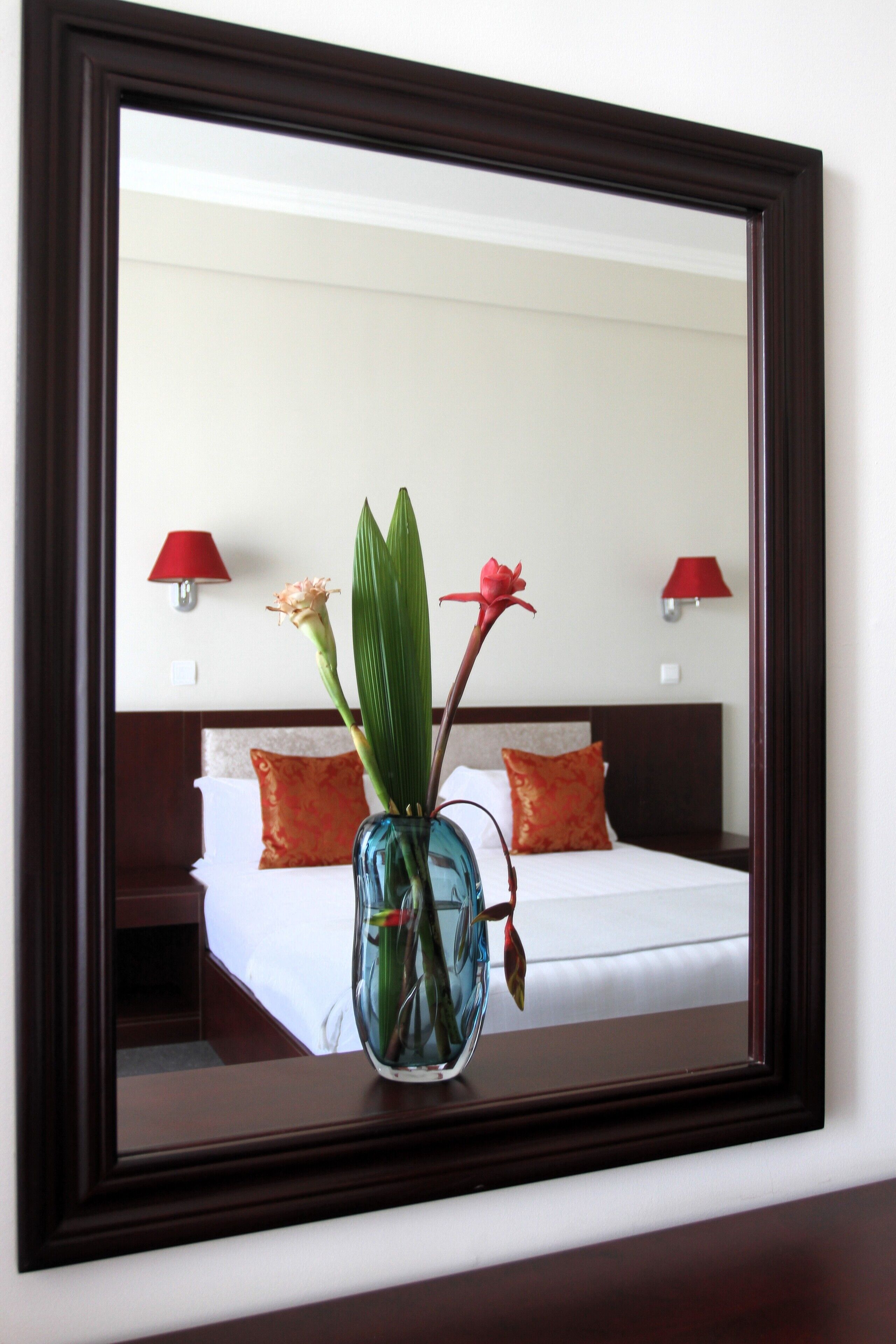 A hotel room with a bed, pillows, a vase with flowers, and two wall lamps.