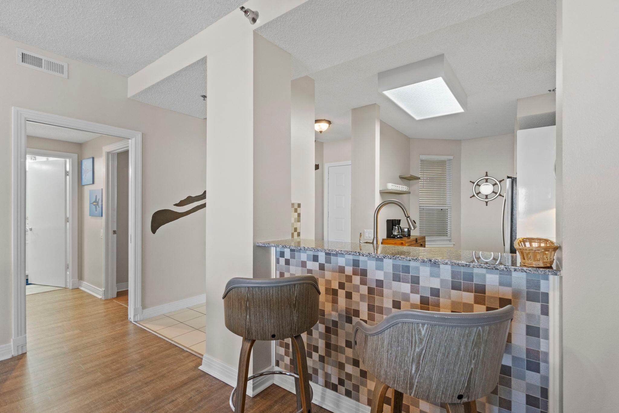 A kitchen with a tiled backsplash, two bar stools, a refrigerator, and a window with blinds.