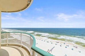 A balcony with a curved railing overlooking a beach with umbrellas and people. - Beach Colony West 11B (Pensacola)