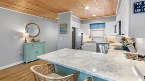 A modern kitchen with a marble island, wooden ceiling, and light blue cabinetry. - Jubilee Landing 206 (Orange Beach)