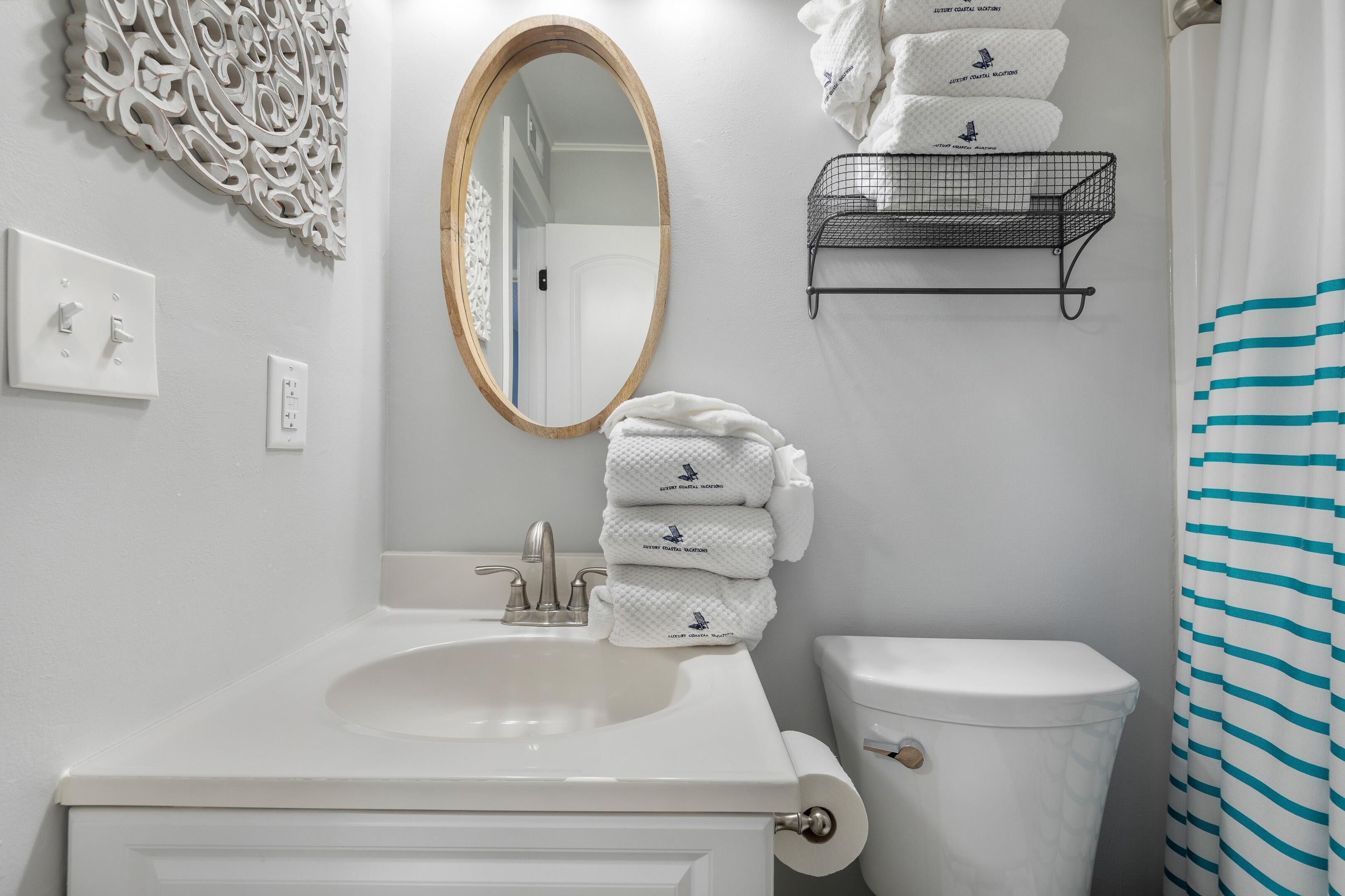 A bathroom with a white sink, a mirror, a toilet, and a towel rack with stacked towels.