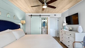 A bedroom with a large bed, a ceiling fan, a dresser, a chair, and a TV on the wall. - Jubilee Landing 206 (Orange Beach)