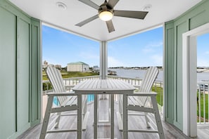 A covered outdoor area with a table and chairs, a ceiling fan, and a view of a body of water and buildings in the distance. - Jubilee Landing 206 (Orange Beach)