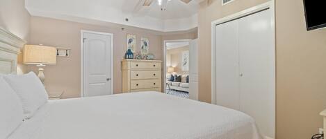 A bedroom with a large bed, a ceiling fan, a dresser, a television, and a door.
