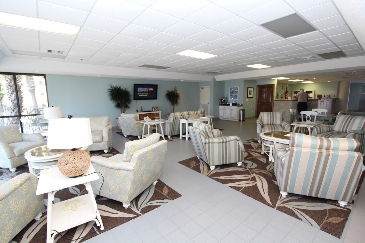 A spacious living area with multiple seating options, a flat-screen TV, and a kitchen area in the background.