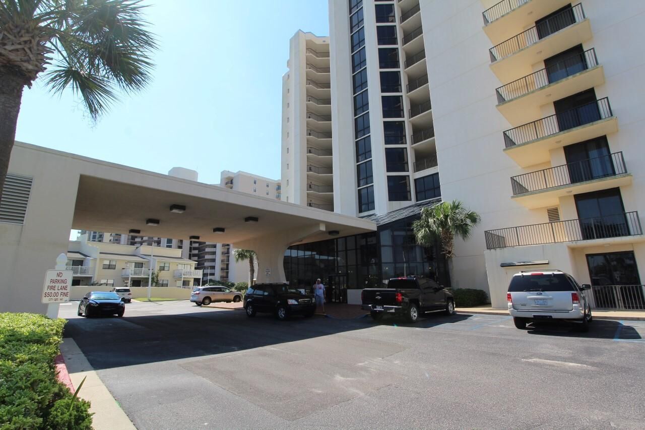 A parking lot with several vehicles, including cars and trucks, in front of a modern building with multiple floors and balconies.