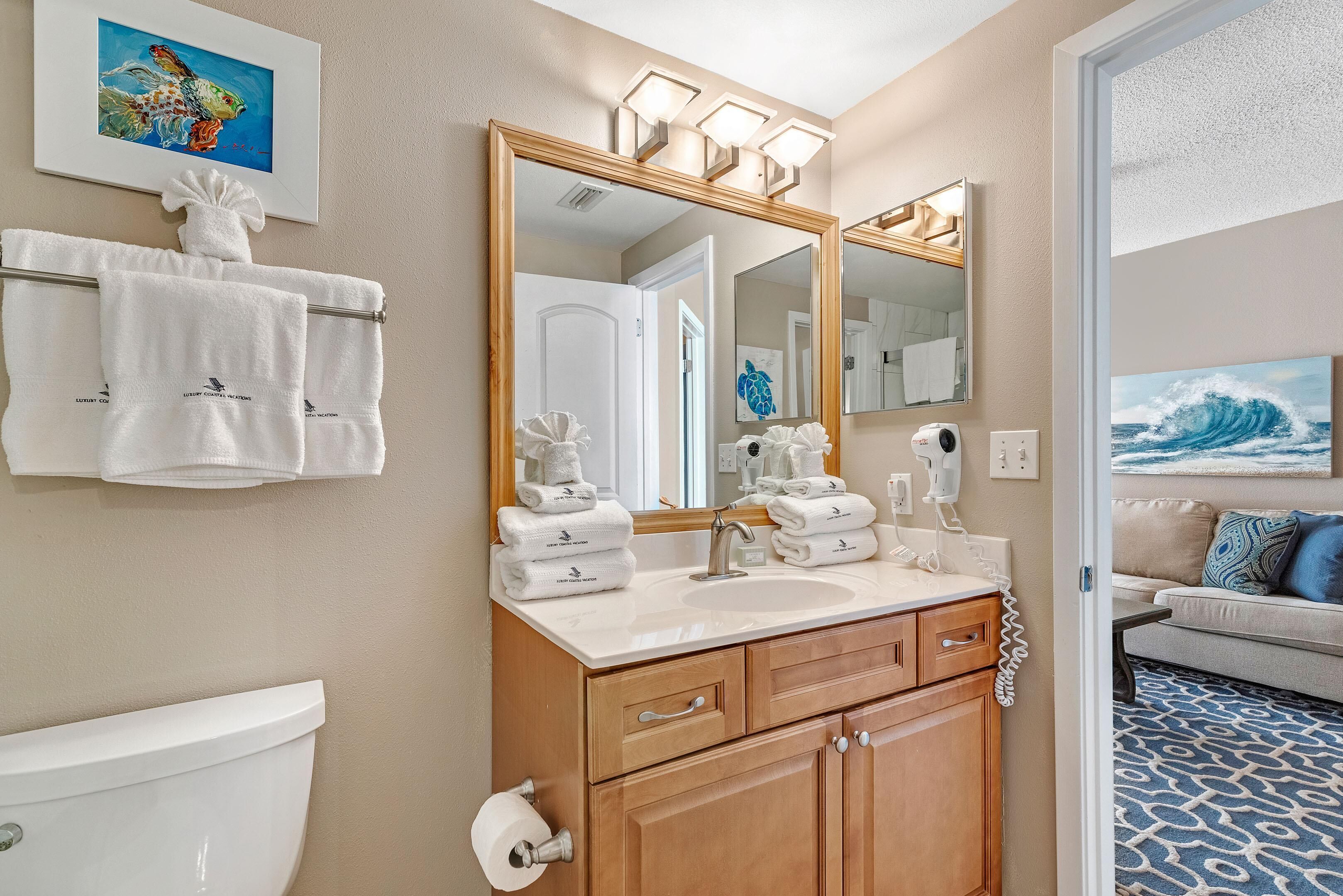 A bathroom with a toilet, sink, and wooden vanity. There are towels on a rack and a mirror above the sink.