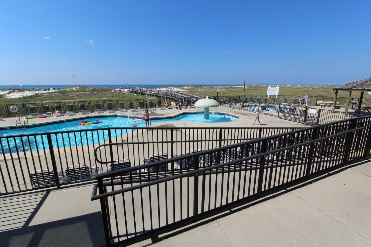 A pool area with a view of the beach, lounge chairs, and a fenced deck.