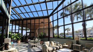 Un intérieur lumineux, baigné de soleil grâce à un plafond en verre, doté de sièges confortables et offrant une vue sur les palmiers et les bâtiments environnants.