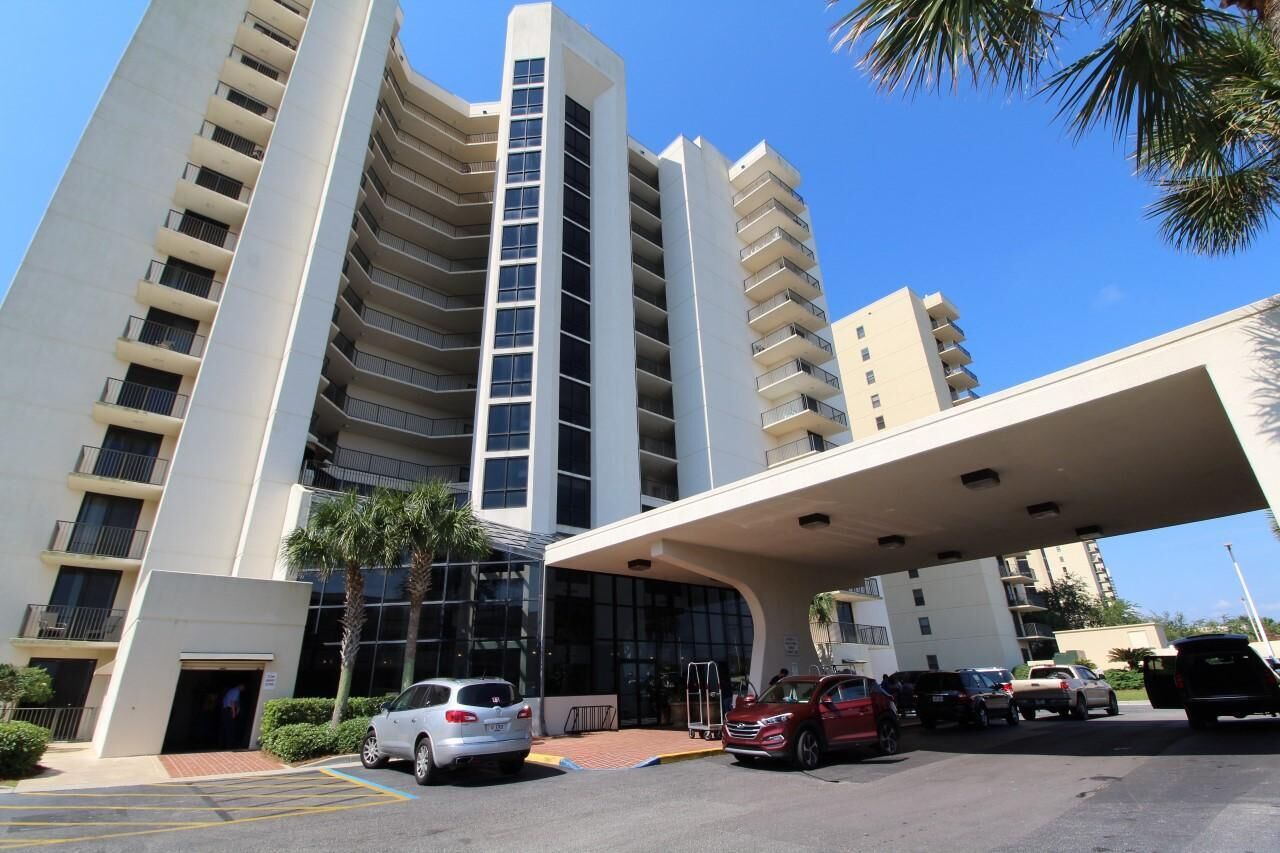 Een modern hotel met meerdere verdiepingen, voorzien van een gebogen entreekap, een parkeerplaats met verschillende auto's, en een helderblauwe lucht.