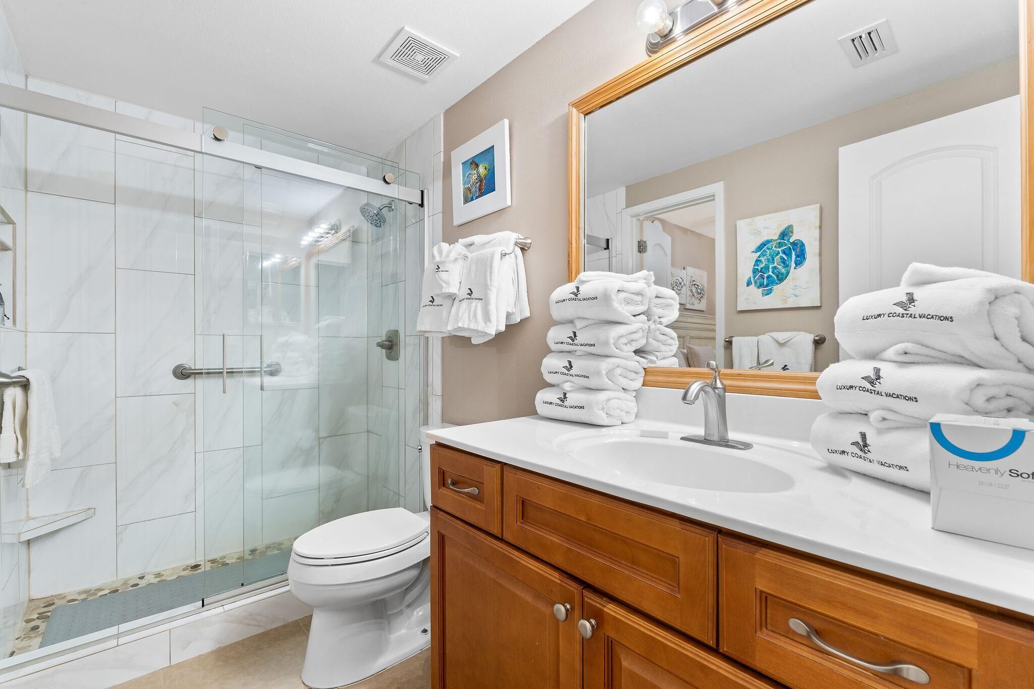 Une salle de bain moderne avec une douche à parois de verre, des toilettes blanches et un meuble-lavabo avec un évier et un miroir. On peut voir des piles de serviettes et un sac rempli de serviettes.